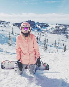 a person sitting in the snow with a snowboard on their feet and wearing goggles