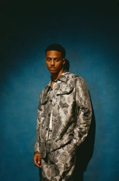 a man standing in front of a blue background wearing a floral print shirt and pants