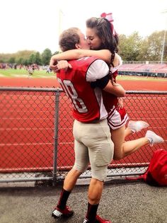 two people are hugging each other in front of a fence at a baseball field,