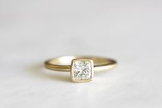 a gold engagement ring with a square cut diamond in the center on a white surface