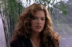 a woman with long curly hair standing in front of a window and looking off to the side