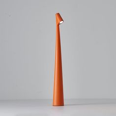 an orange cone shaped light sitting on top of a white table next to a gray wall