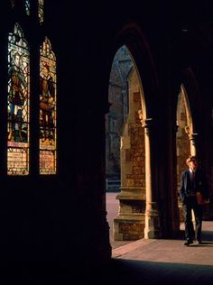 a man in a suit and tie walking through an old building with stained glass windows