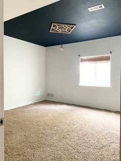 an empty room with carpeted floor and blue painted ceiling above the door is a window