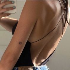 the back of a woman's shoulder with a tattoo on her left arm, holding a cell phone