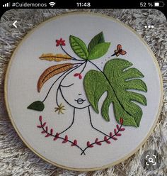 a hand embroidered hoop with a woman's face surrounded by leaves and butterflies