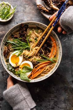 two hands holding chopsticks over a bowl of ramen with an egg on top