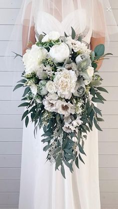 a bride holding a bouquet of white flowers and greenery