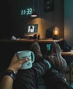 a person holding a coffee mug in their lap while sitting at a desk with a laptop