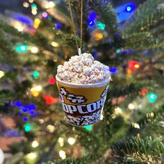 a christmas ornament hanging from a tree with lights in the background and a cup of popcorn on it