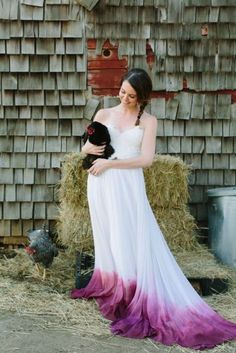 a woman in a white and purple dress holding a black cat next to hay bales