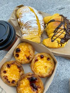 several pastries are in a box next to a cup of coffee and a baguette