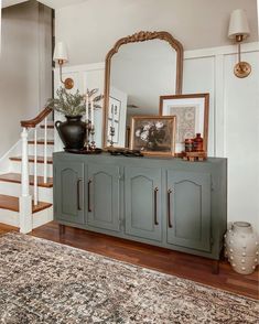 a large mirror sitting on top of a dresser next to a stair case in a living room