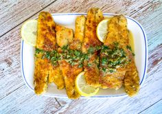 fish fillets on a plate with lemon wedges and parsley garnish