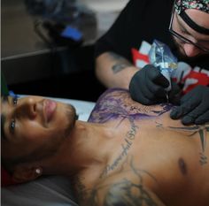 a man is getting his tattoo done by an adult who is wearing black gloves and tattoos