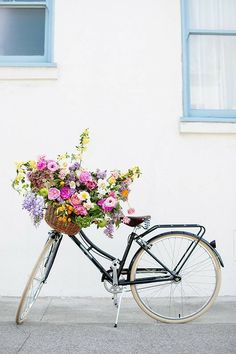 a bicycle with flowers in the basket is parked on the side of the street next to a building