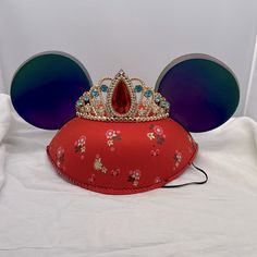 a red mouse ears hat with a tiara on it's head and blue tinted glasses