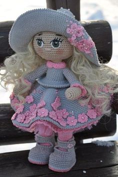 a crocheted doll sitting on top of a bench wearing a hat and dress