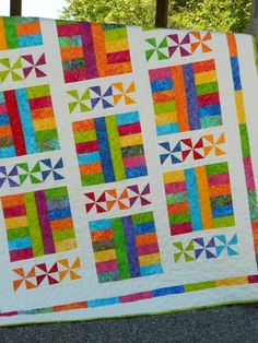 a multicolored quilt is displayed on the ground next to a fence and trees