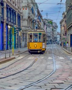 a yellow trolley car traveling down a street next to tall buildings and blue shutters