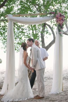 a bride and groom standing under an outdoor wedding ceremony arch with flowers on the altar