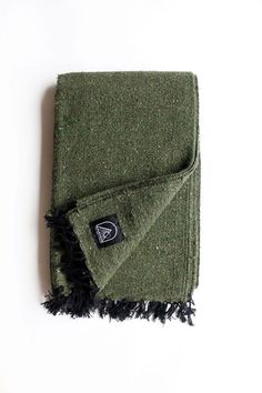 a green blanket with fringes on it and a black patch in the middle that says,