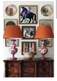 two lamps are sitting on a dresser in front of pictures and other art hanging on the wall