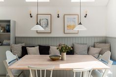 a dining room table with four hanging lights above it and some flowers in a vase on the table