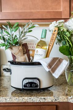 a crock pot filled with food and wine on top of a counter next to flowers