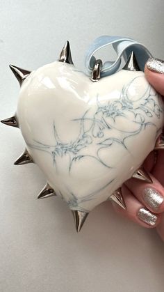 a person holding a white heart shaped object with spikes on it's sides and silver nail tips