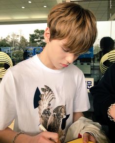 a young boy sitting at a table with a book in front of him and another person standing behind him