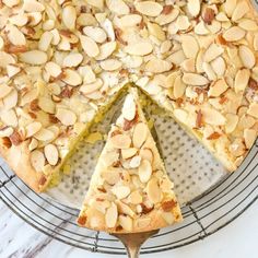 a cake with almonds on top sitting on a wire rack next to a slice missing from it