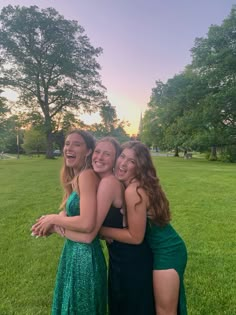 three girls in green dresses hugging each other on the grass with trees in the background