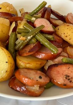 a white bowl filled with potatoes, green beans and sausages on top of each other