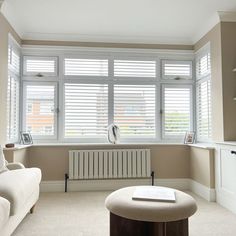 a living room filled with furniture and windows covered in white shuttered glass shades next to a coffee table