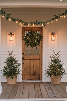 two christmas trees are on the porch next to a door with lights hanging from it