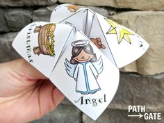 a hand holding two paper angel cards in front of a brick wall