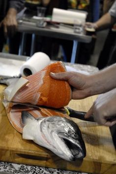 a person cutting up fish on top of a wooden table