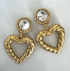 Roped and Beaded Satin Gold Tone Open Heart Drop Clip On Earrings with Round Crystal Glass Foil Back Rivoli Stones in Beaded Setting Cushion Back Clip On Earrings Round Earring Tops with Beaded Edges are Set with Round Faceted Crystal Glass Rivoli Foil Back Stones Roped Open Heart Drops are Crowned with Bead Criss Cross Earrings Measure 2 1/2" Long x 1 1/2" Wide in Center of HeartsRound Earring Tops Measure 3/4" in Diameter Earring Pair Weighs 46 Grams New Vintage From the 1990's Earrings Come in Velvet or Satin Pouch COMPLIMENTARYT DOMESTIC SHIPPING Cross Earrings Vintage, Earring Tops, Rope Heart, Satin Pouch, Round Earring, Earrings Round, Cross Earrings, Open Heart, Faceted Crystal