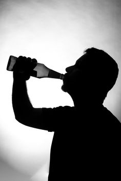 the silhouette of a man drinking from a bottle