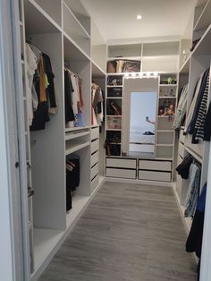 a walk in closet filled with lots of white shelves and clothes hanging on the walls