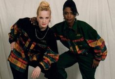 two young women posing for a photo in front of a white backdrop, with one leaning on the other's leg