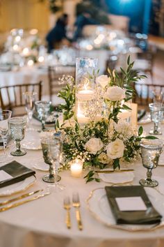 the table is set with silverware, candles and white flowers in centerpieces