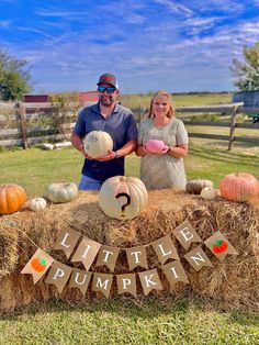 two people standing next to a hay bale with pumpkins on it and the words little pumpkin spelled out