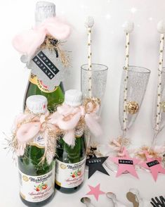 two champagne flutes, one with pink bows and the other decorated with gold stars are sitting next to bottles of champagne