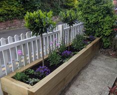 a wooden planter filled with flowers next to a white fence