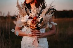 a woman in a white dress holding a bouquet with feathers on her chest and wearing a flower crown