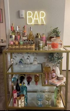 a bar cart filled with lots of bottles and glasses next to a neon sign that says bar