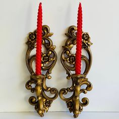 two red candles sitting on top of ornate wall sconces