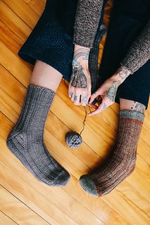 a person sitting on the floor with their feet in socks and holding a ball of yarn